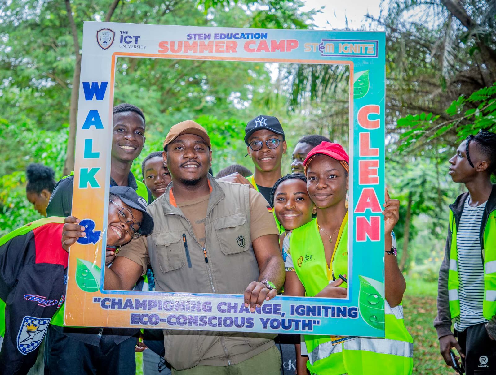 Emmanuel Fru with students holding a STEM Education Summer Camp photo frame outdoors