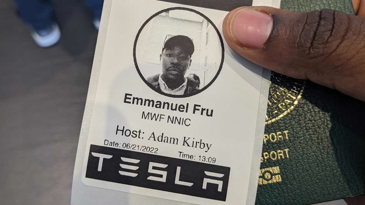 A Tesla visitor badge reading Emmanuel Fru, MWF NNIC, held next to a passport